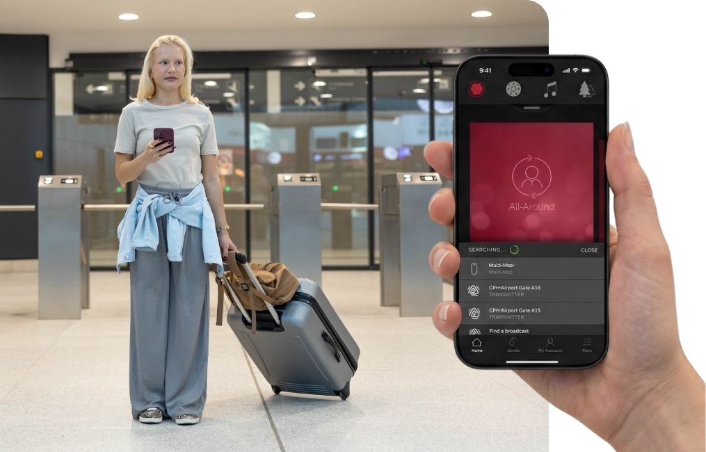 Frau mit Rollkoffer am Flughafen nutzt Smartphone-App zur Steuerung von Resound Hörgeräten in moderner Umgebung​​​​​​​​​​​​​​​​​​​​​​​​​​​​​​​​​​